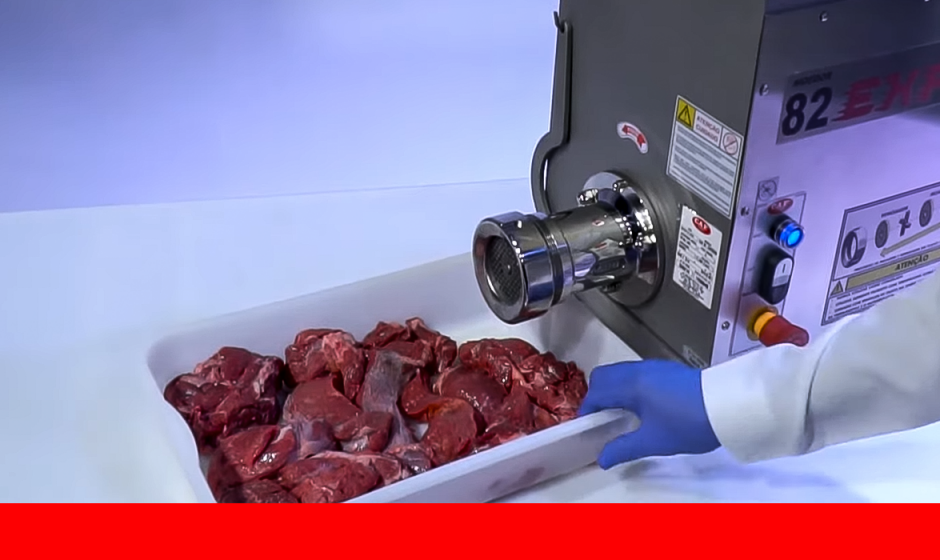 Operador com luva azul posiciona bandeja com pedaços de carne crua em frente a um moedor industrial CAF modelo 82 EXPRESS